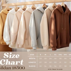Op de afbeelding: Een display van zes hoodies in verschillende neutrale kleuren, waaronder geel, cr&egrave;me, beige, grijs, bruin en donkerbruin, hangend aan houten hangers. Een maattabel voor Gildan 18500 wordt hieronder weergegeven.