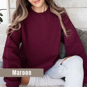 以下が含まれることがあります： マルーンのクルーネックのトレーナー。トレーナーは無地で長袖です。「Maroon」という単語が画像の下部の長方形のボックスに表示されています。トレーナーは柔らかい素材で作られています。
