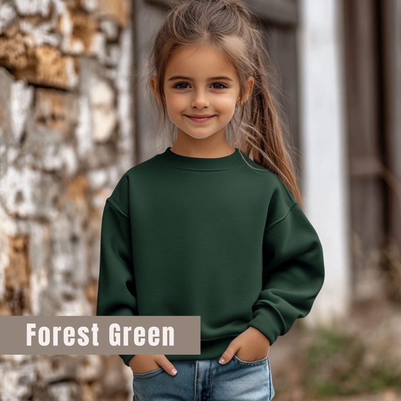 May include: A forest green sweatshirt with a crew neck. The text "Forest Green" is displayed in a rectangular box at the bottom of the image. The sweatshirt is worn by a young person.