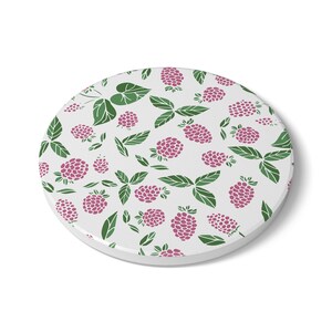 May include: A round, white coaster featuring a repeating pattern of pink raspberries and green leaves. The design is a simple, stylized illustration, perfect for adding a touch of nature to any table setting.