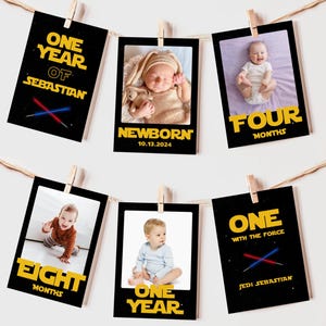 Puede incluir: Una serie de tarjetas fotográficas de hitos para bebés colgadas de una cuerda. Cada tarjeta presenta una foto del bebé y texto que indica la edad, como "Recién nacido", "Cuatro meses" y "Un año". Las tarjetas tienen un borde negro y un tema de Star Wars.