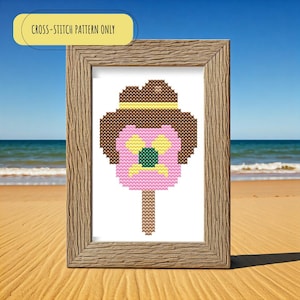 May include: Cross-stitch pattern of a pink ice cream cone with a brown hat and a yellow flower on top. The pattern is framed in a brown wooden frame.