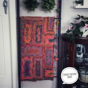 May include: A colorful crochet blanket with a geometric pattern hangs on a black ladder. The blanket is made of a variety of colors, including red, orange, yellow, green, blue, and purple. The blanket is hanging on a black ladder with a string of beads hanging from the top.