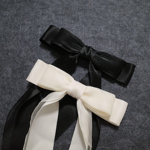 May include: Two hair bows, one black and one white, tied together with the black bow on top. The bows are made of satin ribbon and are tied in a simple knot.