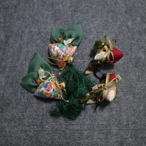 May include: Three colorful fabric pouches with green leaves and tassels. The pouches are decorated with floral patterns and have gold accents.