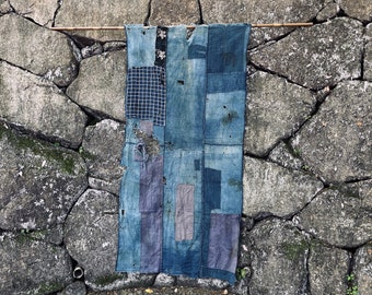 May include: A blue and white patchwork textile hanging on a wall. The textile is made of different pieces of fabric sewn together, creating a unique and textured design.