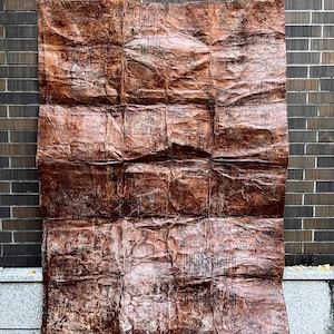 May include: A large, rectangular piece of textured, brown paper with a crinkled appearance. The paper is folded into multiple sections, creating a grid-like pattern. The paper is mounted on a brick wall.