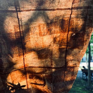 May include: Close-up of a textured, brown paper lantern with a grid-like pattern. The lantern is lit from behind, casting shadows and highlighting the paper's texture. The overall effect is warm and inviting, suggesting a handmade craft.