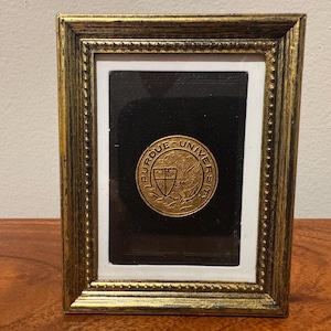 May include: A rectangular picture frame with a distressed gold finish and beaded inner border. Inside, a circular gold-toned Purdue University medallion featuring a shield and griffin emblem is mounted against a black background with a white mat.