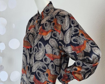 May include: A long-sleeved button-down shirt with a navy blue background and a paisley pattern in beige and orange. The shirt features a classic collar and cuffs, and is displayed on a mannequin.