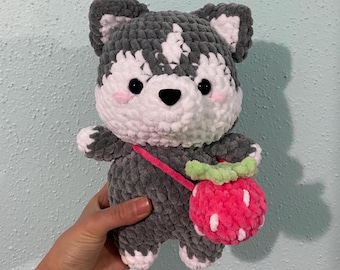 May include: A grey and white crocheted husky plush toy with a pink and white crocheted strawberry attached to a pink strap.