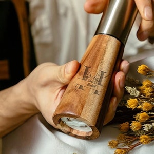 May include: A wooden pepper mill with a stainless steel grinder. The mill is engraved with the letter "H" and the name "Herbert".