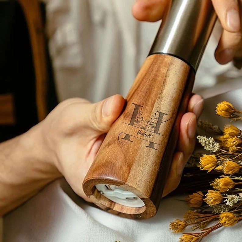 May include: A wooden pepper mill with a stainless steel grinder. The mill is engraved with the letter "H" and the name "Herbert".