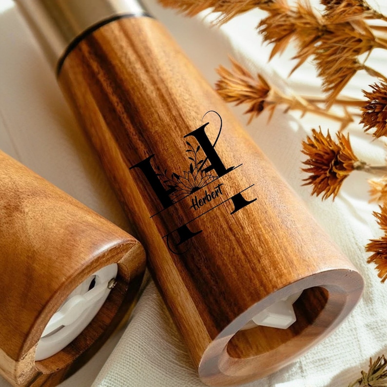 May include: A wooden salt and pepper grinder set with a personalised engraved design. The grinders feature a floral motif and the name "Herbert".