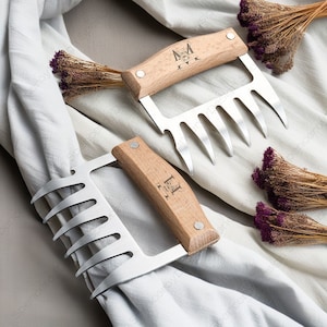 May include: Two meat claws with wooden handles and stainless steel prongs. The handles are engraved with the letters "M" and "H" and the words "With Love" and "Forever".