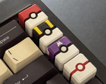 May include: Close-up of a computer keyboard with custom keycaps. The keycaps are designed to resemble various Pokeballs, featuring red, white, black, yellow, and purple colors. The keyboard keys are black and beige.