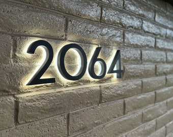 May include: A close-up of a brick wall with a black illuminated house number "2064" mounted on it.
