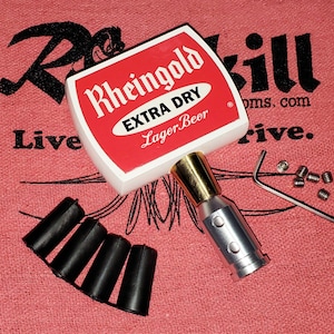 May include: A Rheingold Extra Dry Lager Beer tap handle featuring a white and red rectangular top, a metallic silver and gold connector, four small black rubber inserts, a silver L-shaped hex key, and five tiny silver metal set screws.