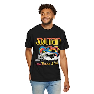 May include: A black short-sleeve t-shirt featuring the yellow text SOULTRAIN above a graphic of a train emitting colorful rainbow smoke. Below the train, the text Love Peace & Soul is printed in yellow, pink, and orange on the front of the shirt.