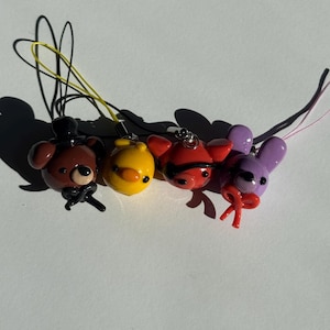 May include: Four colorful character charms. A brown bear with a black top hat and bow tie, a yellow duck, a red fox with a black eye mask, and a purple bunny with a red bow. Each charm has a string for hanging.
