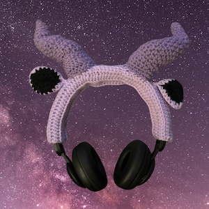May include: Purple crocheted headband with black ear flaps, worn over a pair of black headphones against a starry night sky background.