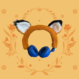 May include: Orange and white crocheted headband with fox ears, featuring blue wireless headphones.