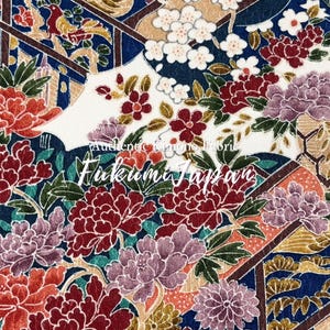 Op de afbeelding: Detail van Japanse stof met een bloemenpatroon. Het ontwerp toont grote rode, paarse en witte bloemen, met groene bladeren en gouden en blauwe accenten. De tekst "Authentic Kimono Fabric" en "Fukumi Japan" zijn zichtbaar.