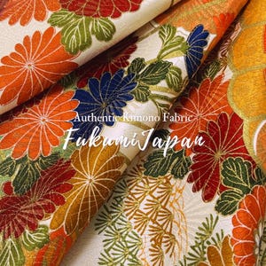 May include: Close-up of authentic Japanese kimono fabric. The fabric features a cream background with a repeating floral pattern in orange, red, blue, and green. The text "Authentic Kimono Fabric Fukumi Japan" is visible.