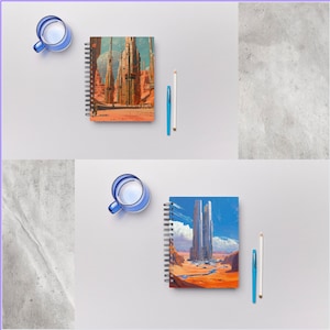 Op de afbeelding: Twee spiraalgebonden notitieboekjes met kleurrijke omslagen met futuristische stadsgezichten. De omslagen zijn een mix van oranje, bruin, blauw en wit. De notitieboekjes liggen op een wit oppervlak met een blauwe glazen beker en een wit potlood.