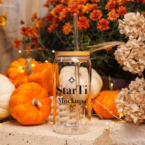 May include: A clear glass tumbler with a bamboo lid and straw, featuring the text "StarTi Mockups." The tumbler is surrounded by orange pumpkins, white pumpkins, and fall foliage, creating a seasonal autumn theme.
