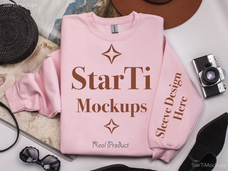 Pu&ograve; includere: Una felpa rosa con il testo "StarTi Mockups" e "Sleeve Design Here" stampato su di essa. La felpa &egrave; stesa su una superficie bianca con altri oggetti intorno.