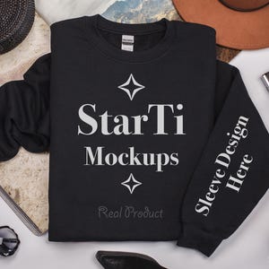 Pu&ograve; includere: Mockup di felpa nera con il testo "StarTi Mockups" e "Sleeve Design Here" sulla manica. La felpa &egrave; stesa su una superficie bianca con altri accessori.