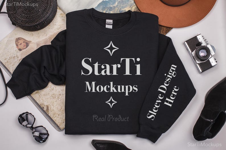 Pu&ograve; includere: Mockup di felpa nera con il testo "StarTi Mockups" e "Sleeve Design Here" sulla manica. La felpa &egrave; stesa su una superficie bianca con altri accessori.
