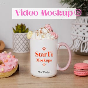 Puede incluir: Taza de cerámica blanca con asa rosa, llena de crema batida y chispas de chocolate. La taza tiene el texto "StarTi Mockups Real Product" impreso en ella. La taza está sobre una mesa de madera con una dona rosa y dos macarons.