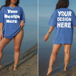 May include: A woman wearing a blue oversized t-shirt with the text "Your Design Here" printed on the front and back. She is standing on a sandy beach with water in the background.