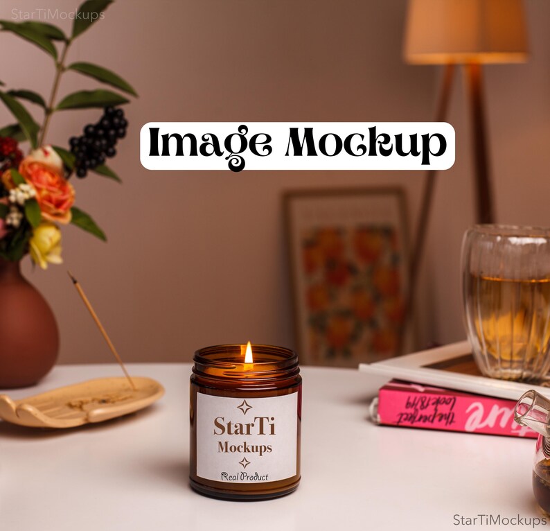 May include: A brown glass candle jar with a white label that reads "StarTi Mockups Real Product" and a lit candle inside. The candle is on a white table with a wooden incense holder and a pink book.