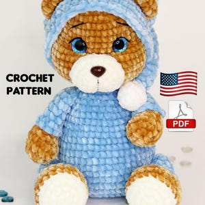 Op de afbeelding: Een gehaakte teddybeer in een lichtblauwe outfit en bijpassende capuchon. De beer heeft bruine vacht, witte accenten en blauwe ogen. De afbeelding bevat de tekst "CROCHET PATTERN" en een PDF-pictogram.