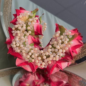 May include: A pink and red flower crown with white pearl and crystal beads. The crown is made of silk flowers and is ideal for a wedding or special occasion.