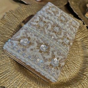 May include: A white clutch bag with gold and silver sequins and beads in a geometric pattern.
