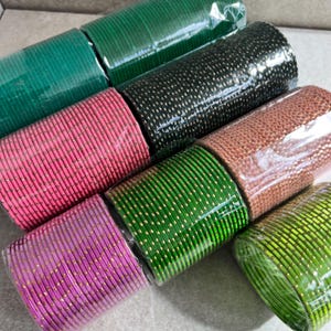 May include: A collection of colorful bangles in various shades, including green, pink, and purple, wrapped in clear plastic. The bangles have a metallic sheen and are arranged in neat rows, showcasing a variety of colors and textures.