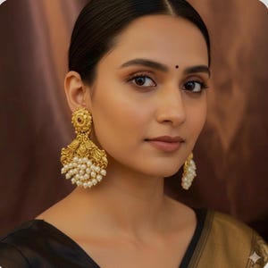 Peut inclure: Boucles d'oreilles pendantes dorées avec un motif floral et de petits accents de perles. Les boucles d'oreilles présentent un motif orné et une petite pierre rouge. Bijou de déclaration.