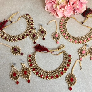 May include: Three gold-tone Indian bridal jewellery sets with red and pink stones. Each set includes a necklace, earrings, and a tikka.