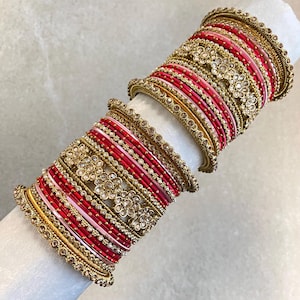 May include: A set of stacked bangles featuring alternating thin red, pink, and gold bands. Several bangles are embellished with intricate gold-tone floral patterns and small clear stones, while others have a smooth, solid metallic finish.