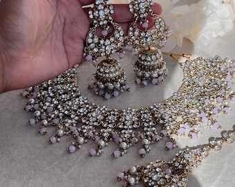 May include: A gold and white bridal necklace set with pink beads and a matching pair of earrings. The necklace features a layered design with multiple strands of beads and a large pendant in the center. The earrings are long and dangle, with a similar design to the pendant.