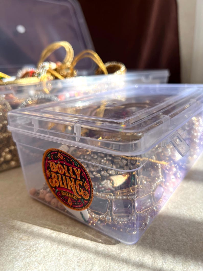 May include: Clear plastic storage containers filled with jewelry. The containers have lids and are filled with necklaces, bracelets, and other accessories. One container has a sticker that says "Bolly Bling Bazaar".