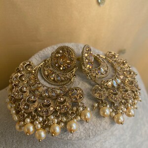 Peut inclure: Une paire de boucles d'oreilles en or avec un motif de croissant de lune et des accents de perles. Les boucles d'oreilles sont orn&eacute;es de strass scintillants.