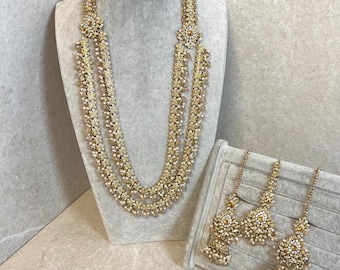 Puede incluir: Un collar de varias capas en oro y blanco con un juego de pendientes a juego. El collar tiene un diseño floral y los pendientes tienen forma de lágrima.