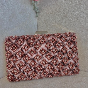 May include: A rectangular clutch bag with a geometric pattern of small, round, rose-coloured beads. The beads are arranged in a diamond pattern with silver lines. The bag has a silver clasp.