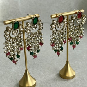 May include: A pair of gold-tone dangle earrings with a pearl and gemstone design. The earrings feature a large green and red stone at the top, followed by a circular design with smaller stones, and then a cascade of pearls and smaller green and red stones.