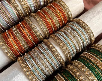 Peut inclure: Plusieurs bracelets colorés, notamment orange, vert et bleu, sont présentés sur un tissu blanc. Les bracelets présentent des motifs complexes avec du métal doré et des ornements décoratifs, mettant en valeur diverses textures et motifs.